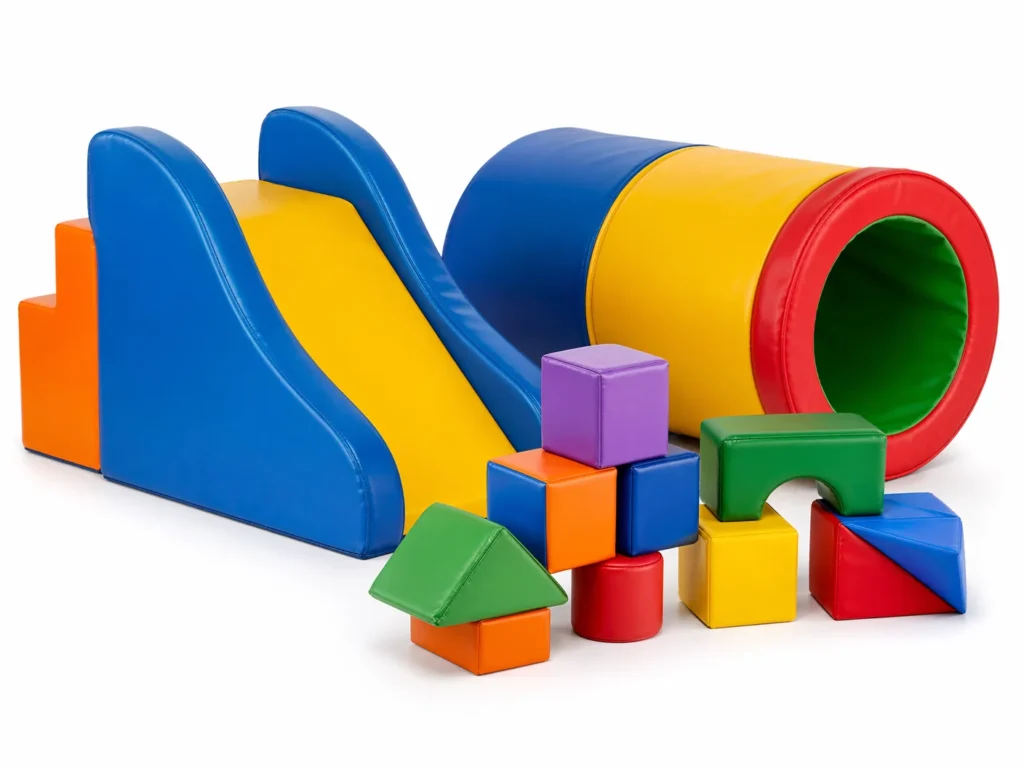 A collection of commercial soft play equipment for toddlers: a small foam slide, a crawling tunnel, and soft building blocks. High-quality product photography, clean white background, vibrant but professional colors, showing the texture of the high-density foam and vinyl covering.