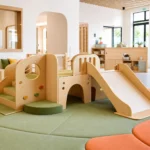 Commercial daycare indoor playroom with a low wood playground climber, soft mats, and clear supervision sightlines