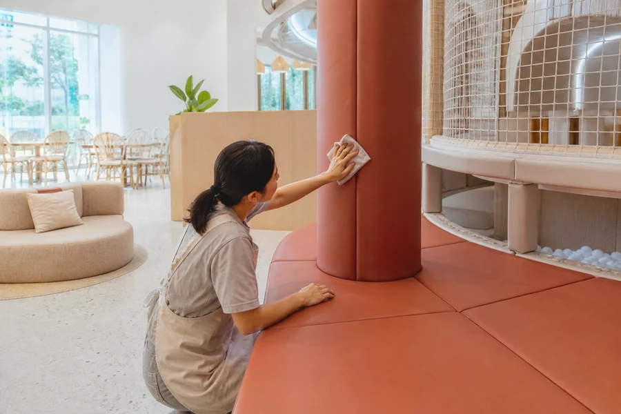 Staff member wiping a PVC-covered soft play column and padded deck in a commercial play cafe.